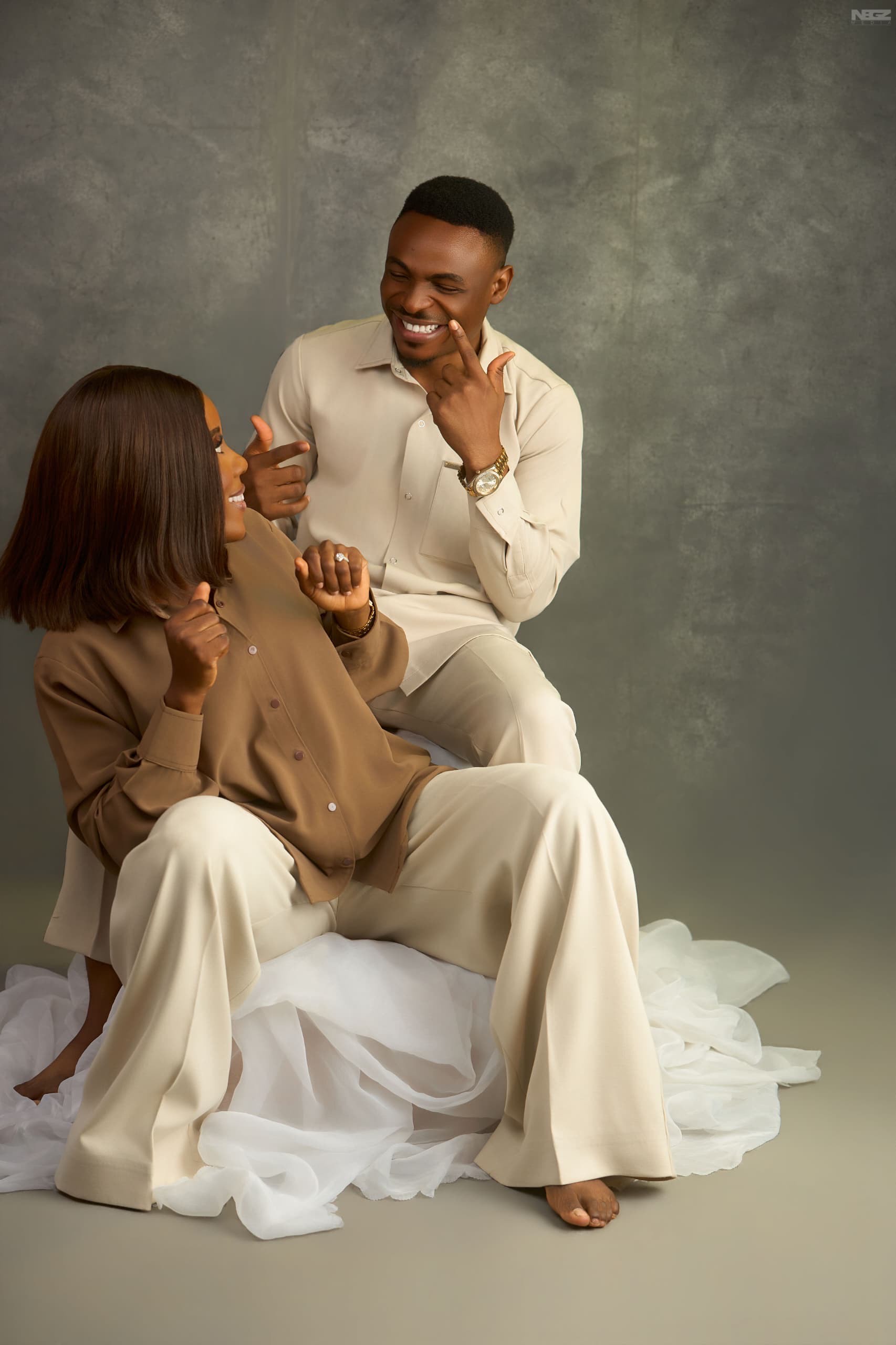 James and Edi laughing together, seated close on a bed of ivory tulle